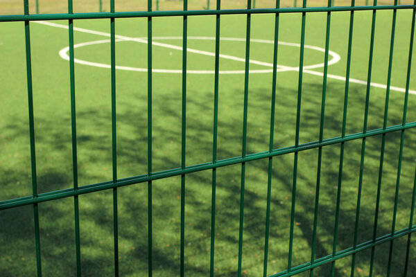 лужайка для игры в мини-футбол за зеленой сеткой забора
