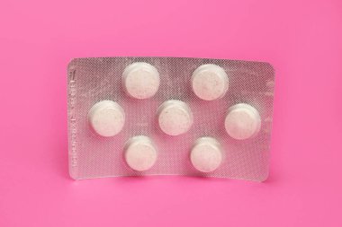 Büyük yuvarlak tabletler, pembe arka planda su toplamış vitaminler.