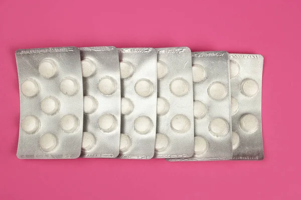 Large round tablets, vitamins in a blister on a pink background