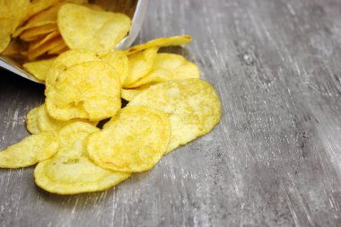 Gri arka planda ambalajdan saçılmış patates cipsleri