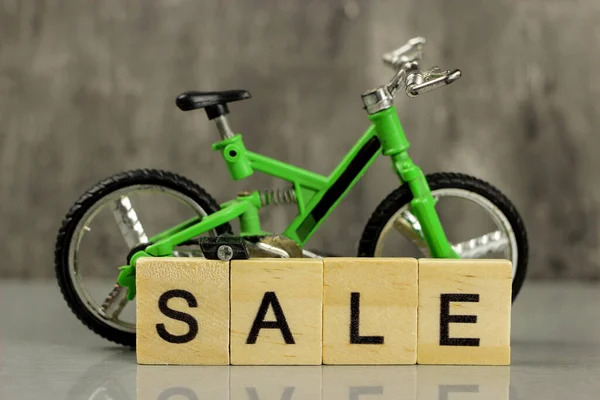 Toy model green full-suspension mountain bike on a gray background and the word Sale