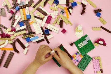 Pembe arka planda renkli bloklarla oynayan çocuk, elleri yakın plan