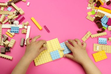 Renkli bloklarla oynayan bir çocuğun elleri, pembe arka planda tuğlalar.