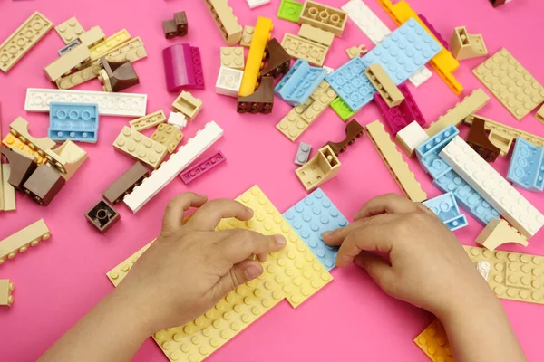 Hands of a child playing with colored blocks, bricks on a pink background