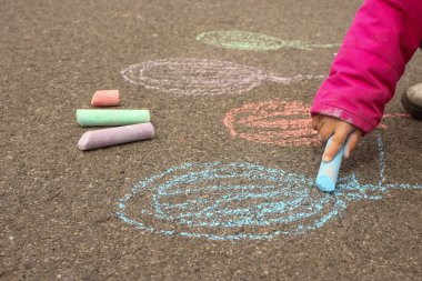 Çocuk kaldırıma tebeşirle renkli balonlar çiziyor.