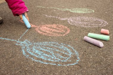 Çocuk kaldırıma tebeşirle renkli balonlar çiziyor.