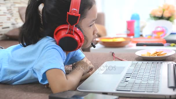 Primer plano de niña asiática usando ordenador portátil y auriculares en casa — Vídeos de Stock