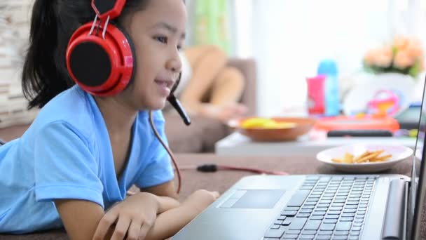 Primer plano de niña asiática usando ordenador portátil y auriculares en casa — Vídeos de Stock