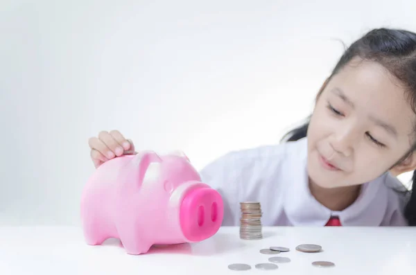 Asian little girl in Thai student uniform putting coins to piggy — Stock Photo, Image