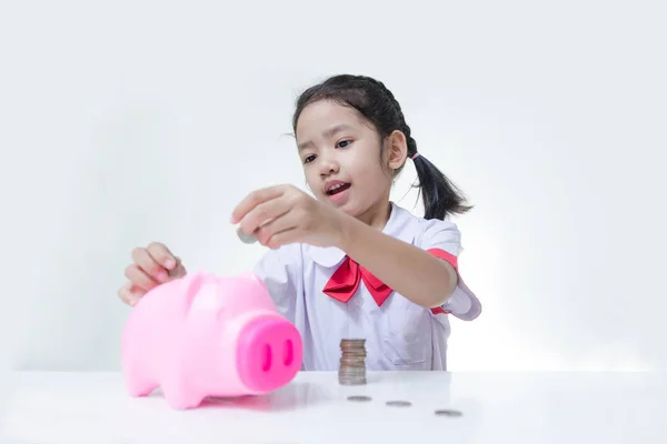 Asian little girl in Thai student uniform putting coins to piggy — Stock Photo, Image
