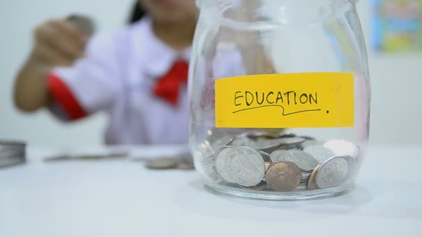 HD-Primer plano de niña asiática en uniforme de estudiante tailandés con monedas y frasco de vidrio ahorrando dinero concepto — Vídeos de Stock