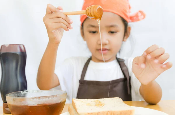 Asiática niña sostener la miel cazo a un pan — Foto de Stock