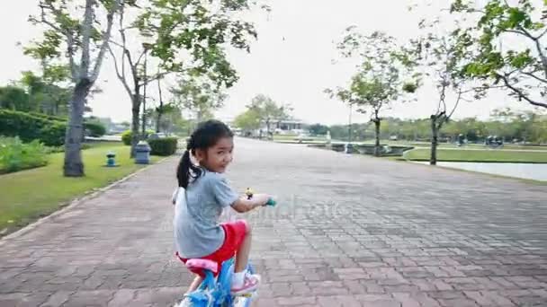 Asyalı küçük kız kamera takipçisi ile kamu parki bir bisiklet sürme — Stok video