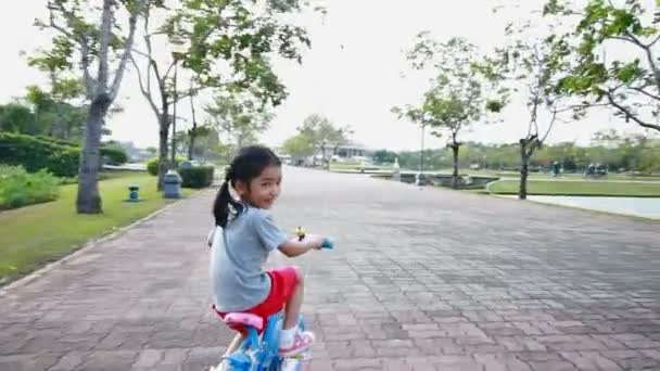 Asiatico bambina equitazione un bicicletta in pubblico parco con macchina fotografica follower — Video Stock