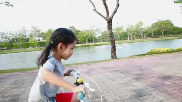 Asiática niña montando una bicicleta en el parque público con la cámara seguidor — Vídeos de Stock