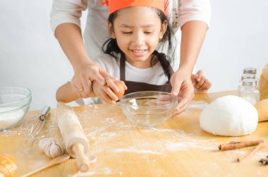 Asyalı küçük kız anne için yumurta kabuğu kırma görüntüsünü kapatmak