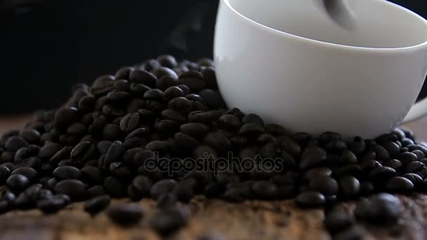 Primer plano plano de granos de café tostados oscuros caen en la taza de cerámica blanca en el suelo de madera con el color de tono oscuro graduado — Vídeo de stock