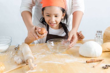 Asyalı küçük kız anne için yumurta kabuğu kırma görüntüsünü kapatmak