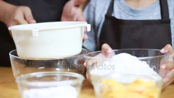 Close up shot Mãos de mãe e filha estão peneirando farinha e misturando ingredientes para assar — Vídeo de Stock