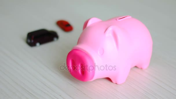 Close up tiro mão de homem colocando dinheiro moeda em rosa porquinho banco e carro borrão por trás metáfora de poupar dinheiro para comprar o conceito de carro — Vídeo de Stock