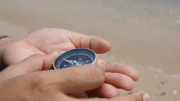 De cerca la mano de disparo de la mujer utilizando una brújula en la playa de arena con la naturaleza de la costa del mar — Vídeos de Stock