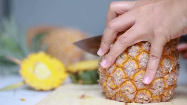Закройте руки женщин, использующих кухонный нож, чтобы резать и очищать спелые ананасы мелкой глубины поля с окружающим звуком — стоковое видео
