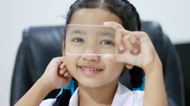 Крупный план Азиатская маленькая девочка в тайском детском саду студенческая униформа с использованием прозрачного стекла так же, как смартфон со счастьем для футуристических кибертехнологий концепции подключения к сети — стоковое видео