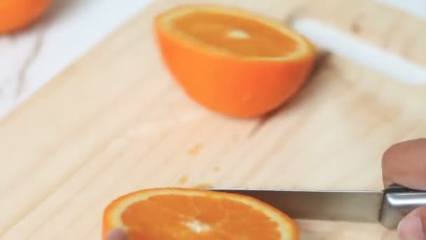 Cerca de tiro manos de la mujer usando cuchillo de cocina para cortar corte de naranja fresca y madura en madera tabla de cortar profundidad superficial de campo — Vídeo de stock