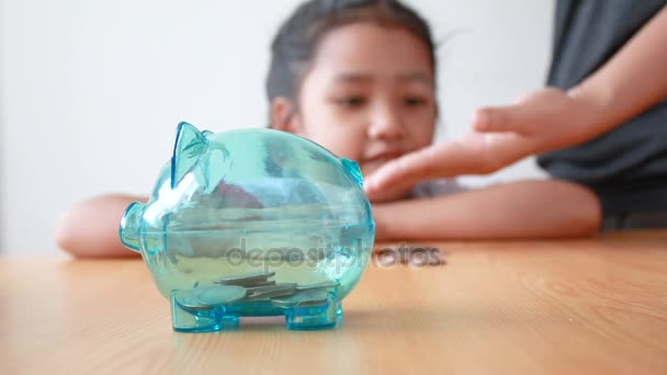 투명 돼지 저금통에 돈을 동전을 넣어 타이어 유치원 학생 유니폼에 아시아 소녀 선택 돼지 앰비언트 사운드 교육 개념에 대 한 비용을 절약에 초점 — 비디오