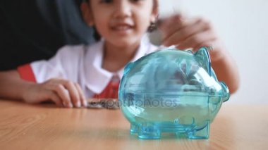 Asyalı küçük kız Tay anaokulu öğrencisi üniformalı para sikke açık kumbara koyarak seçin odak eğitim kavramı için para tasarrufu domuz