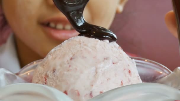 Zblízka střílel Asijská holčička pomocí lžíce nalévání kapalin čokoládová poleva na kopeček zmrzliny — Stock video