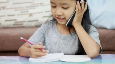 Çekim Asyalı küçük kız ödev kalem kullanarak kapatın ve Smartphone-e doğru konuşmak