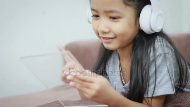 Азиатская маленькая девочка, использующая белый беспроводной наушник и чистую площадку для футуристических технологий — стоковое видео