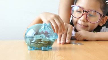 küçük kız Tay anaokulu öğrenci üniforma içine koyarak para sikke sian temizleyin kumbara ahşap masa mecaz para tasarrufu için eğitim kavramı üzerinde