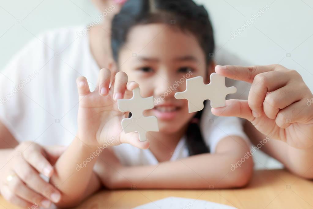 Asian little girl playing jigsaw puzzle with her mother for fami