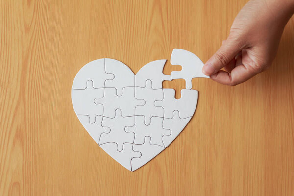 Close up shot hand of woman playing jigsaw puzzle on wooden tabl