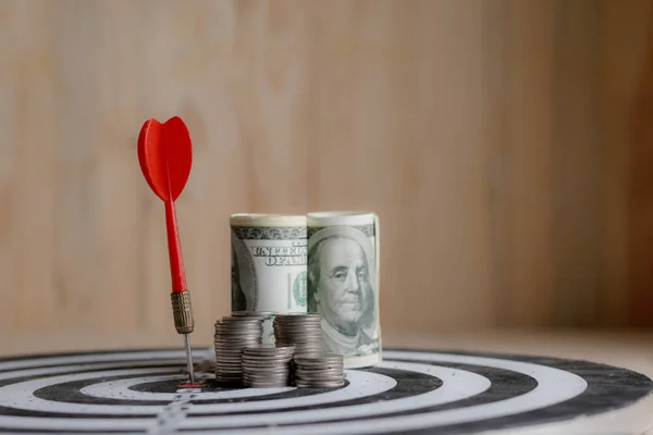 Red dart arrow hit the center target of dartboard and money coin — Stock Photo, Image