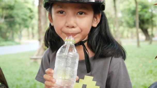 可爱的亚洲小女孩穿着粉红色的头盔饮用水与幸福的自然公园 — 图库视频影像