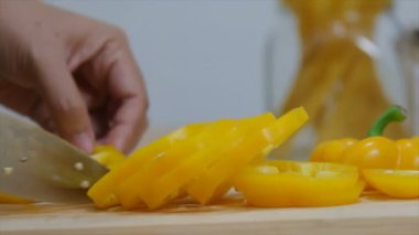 Kadının elleri mutfak bıçağı dilimi ve çan biberini keserek yemek pişirmeye hazırlanıyor.