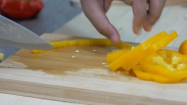 Kadının elleri mutfak bıçağı dilimi ve çan biberini keserek yemek pişirmeye hazırlanıyor.