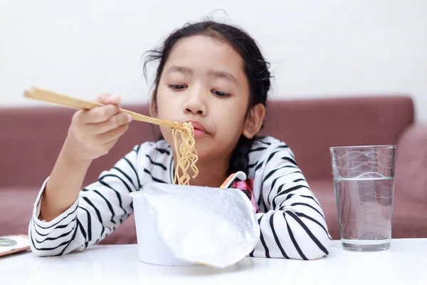 Маленькая азиатка сидит за белым столом и ест лапшу. — стоковое фото