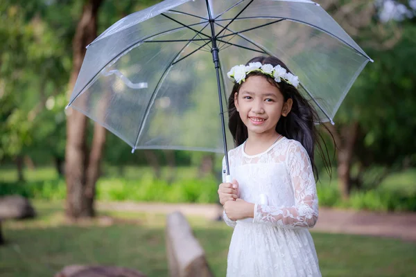 亚洲小女孩拿着一把清晰的雨伞，带着幸福的笑容 — 图库照片