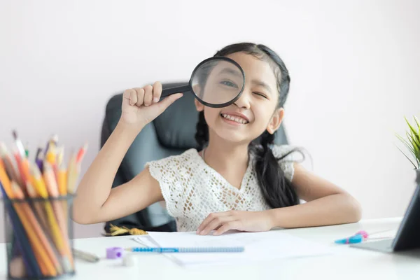 Pequeña chica asiática usando lupa haciendo tarea y sonrisa con —  Fotos de Stock