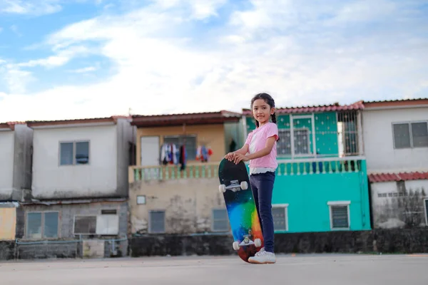 Asiática niña sosteniendo monopatín y sonrisa con felicidad a — Foto de Stock