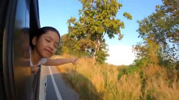 亚洲小女孩把头伸出车窗 带着愉快的笑容 带着夜晚的自然光 准备上路或旅行 — 图库视频影像