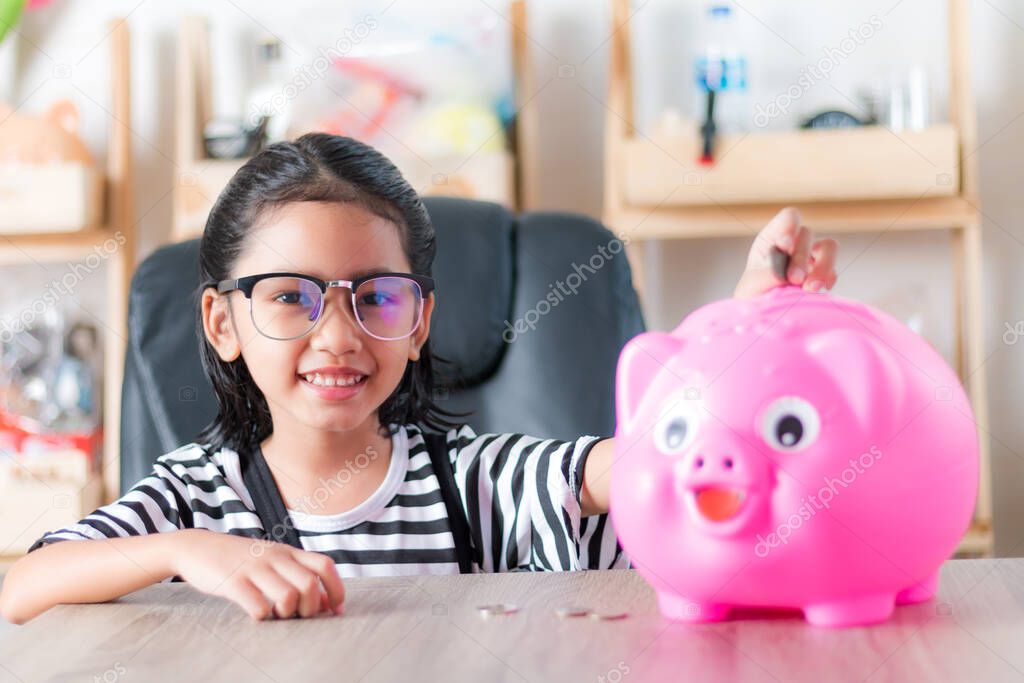 Asian little girl in putting coin in to piggy bank shallow depth of field select focus at the face