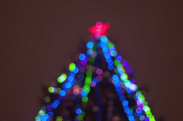 Christmas tree on the street, decorated with a garland, in defocus.