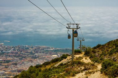 Kablolar, direkler, dağlar, ayaklarının altındaki şehir.