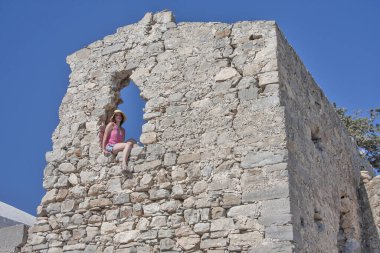 Antik bir duvarın boşluğunda oturan kız.