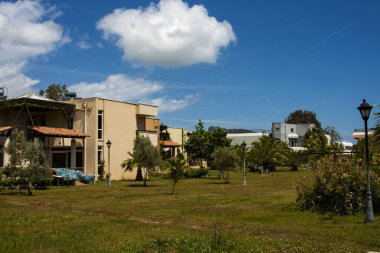 Kulübeler, çimenler, yeşil ağaçlar ve mavi gökyüzü